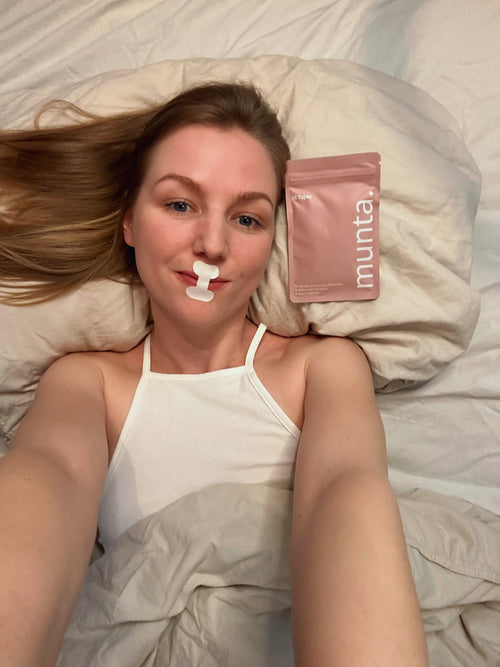 Eine Frau liegt entspannt im Bett mit Munta Mundpflaster auf den Lippen -  Mouth Taping für besseren Schlaf